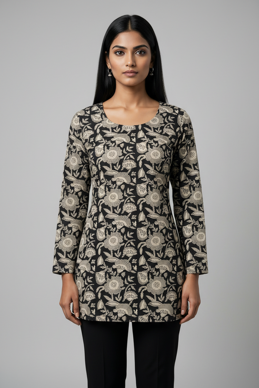A woman stands in a modern office setting wearing a long-sleeve tunic top with a black, beige, and white floral pattern, paired with black pants.