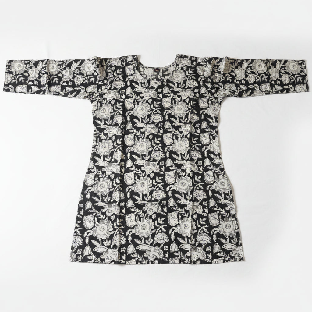 A long-sleeved batik shirt with a black and white floral pattern, laid flat on a bright green background.