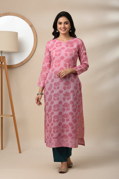 A pink long-sleeve shirt with a pink floral pattern, laid flat on a bright green sheet. A blue and white tag is visible on the chest.