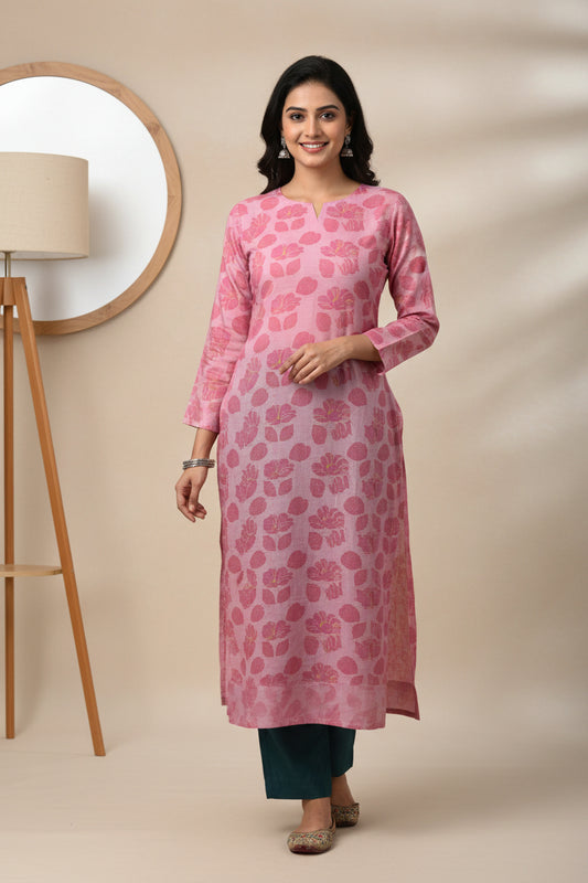 A pink long-sleeve shirt with a pink floral pattern, laid flat on a bright green sheet. A blue and white tag is visible on the chest.
